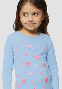 T-shirt à manches longues bleu avec des motifs de cœurs roses brillants et multicolores dispersés sur le devant, fabriqué en coton doux.