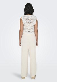 Top blanco de crochet con bordes en forma de concha y mangas cortas, combinado con pantalones de pierna ancha en beige claro y zapatos de esparto.