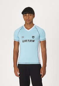 Ανοιχτό μπλε αθλητικό μπλουζάκι με V-neck, μαύρες λεπτομέρειες, κοντά μανίκια, και το κείμενο "URTRN" μπροστά. Αριθμός "32" στο αριστερό στήθος.