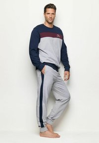 Sudadera gris con rayas en azul marino y burdeos, con el texto "FEEL GOOD". Pantalones de chándal grises con rayas laterales en azul marino y puños acanalados.