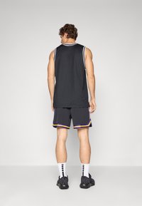 Camisola sem mangas preta e calções pretos com detalhes em roxo e amarelo, combinados com meias brancas às riscas e sapatilhas pretas.