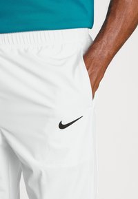 Weiße Nike-Shorts verfügen über einen dehnbaren Bund, eine eingearbeitete Tasche und ein schwarzes Logo am linken Bein. Der Stoff hat eine glatte Textur.