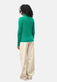 Maglione verde a maglia con colletto alto, polsini a costine e silhouette aderente. Abbinato a pantaloni larghi color crema.