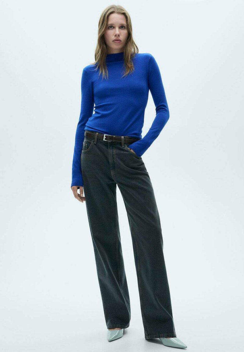 Modra pletena majica z dolgimi rokavi, kombinirana z visokim pasom in širokimi temnosivimi kavbojkami. Manekenka nosi svetlo modre špičaste čevlje. Enostavna ozadje.