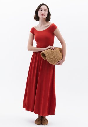 Abito maxi rosso, con spalle scoperte, in tessuto testurizzato, vita cintrata e gonna fluente. Completato da una pochette intrecciata marrone e scarpe slip-on.