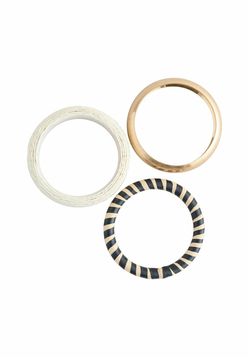 Tre ringe: en tyk hvid tekstureret band, en glat guldband og en ring med sort-hvide striber. Forskellige materialer og overfladebehandlinger.