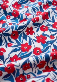 Tejido de algodón con un patrón floral que presenta flores rojas y hojas azules sobre un fondo blanco, textura suave con un acabado liso.
