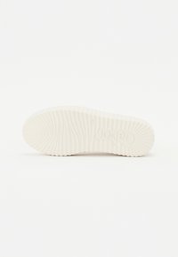 Semelle de chaussures en caoutchouc blanc avec des rainures verticales et un logo en relief. La surface légèrement texturée améliore l'adhérence et la traction.