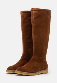 Brown suede knee-high boots with a flat sole, smooth texture, and a side zipper. Features a rounded toe and stitched detailing.