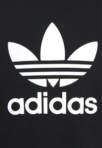 Tessuto nero con un grande logo Adidas trefoil bianco, caratterizzato da tre foglie e tre strisce orizzontali sopra il nome del brand in minuscolo.