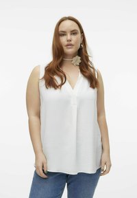 Haut sans manches blanc avec une surface texturée et un col en V. Associé à un jean taille haute bleu. Souligné par un collier choker florale.
