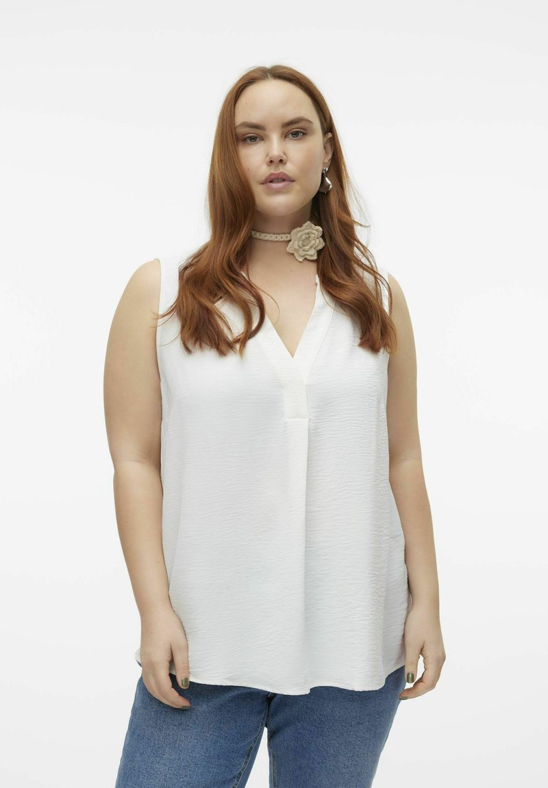 Haut sans manches blanc avec une surface texturée et un col en V. Associé à un jean taille haute bleu. Souligné par un collier choker florale.