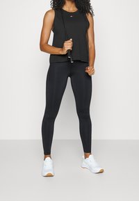 Canotta atletica nera con scollatura rotonda, abbinata a leggings neri a vita alta e sneakers bianche con suola in gomma. Corda in mano.