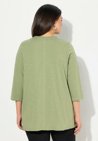 Olivově zelený top s tříčtvrtečními rukávy, kulatým výstřihem a kontrastním prošíváním. Hladká textura, delší zadní lem a ležérní design.