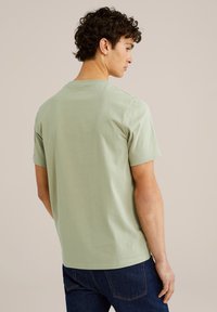 Žali medvilniniai marškiniai trumpomis rankovėmis, su apvaliu iškirpimu, lygaus paviršiaus ir paprasto dizaino, matomi iš nugaros. Nėra jokių raštų ar akcentų.