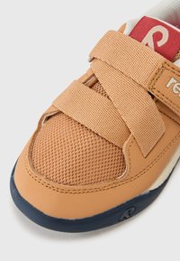 Beige Sneaker mit einem Mesh-Obermaterial und synthetischen Überzügen. Verfügt über Klettverschlüsse und eine marineblaue Gummisohle. Rote Markierungsdetails an der Ferse.