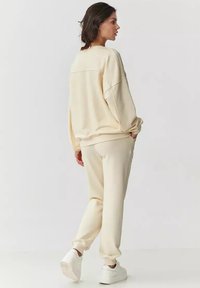 Jasnobeżowy zestaw odzieży domowej wykonany z miękkiego materiału. Bluza ma luźny krój, opadające ramiona i ściągacze na mankietach; spodnie mają elastyczne mankiety.