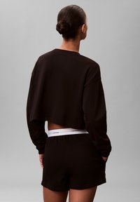 Czarna krótka bluza z długimi rękawami, zestawiona z czarnymi szortami z białym pasem w talii z napisem "Calvin Klein". Miękka faktura, casualowy krój.