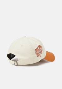 Beige cotton baseball cap with an orange visor, featuring an embroidered "World Series" logo in multicolor on the back. Adjustable metal clasp.