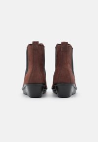 Bottines en daim marron avec des panneaux latéraux élastiques et un talon noir brillant. Caractéristiques d'une texture lisse et de lignes épurées pour un look moderne.