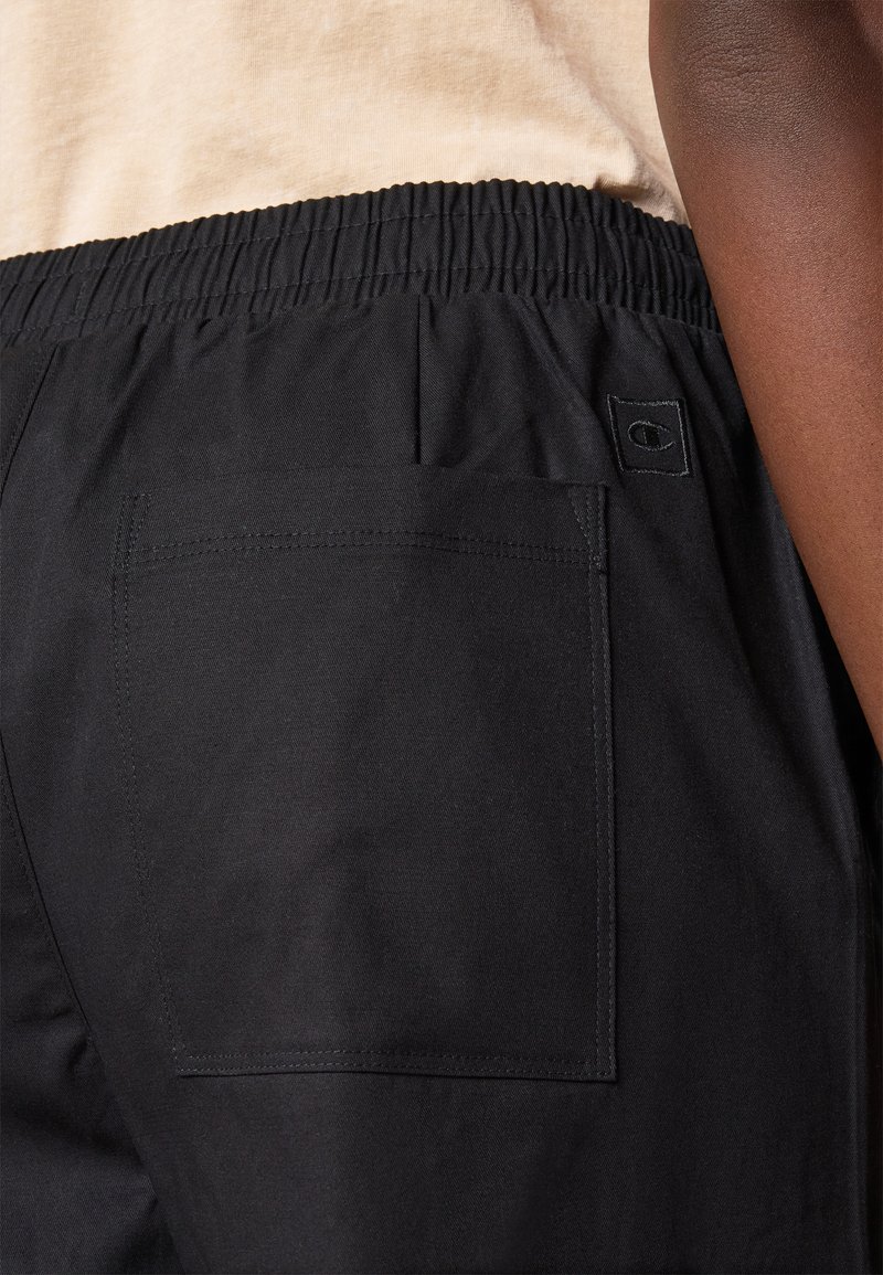 Pantaloni corti neri con elastico in vita realizzati in un tessuto dalla superficie liscia. Presentano una tasca posteriore e un piccolo logo su etichetta nella cintura.