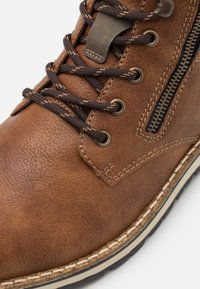 Bota de cuero marrón con un acabado texturizado, que presenta cordones marrones, ojales de bronce, un zipper lateral y una suela con costura blanca en contraste.