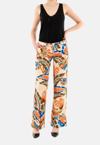 Pantalons larges à fleurs avec un fond crème, ornés de motifs tropicaux vibrants en orange, bleu et vert, associés à un débardeur noir.