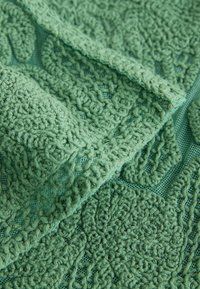 Gros plan sur un tissu vert texturé avec des motifs formant des boucles en relief sur un fond en maille.