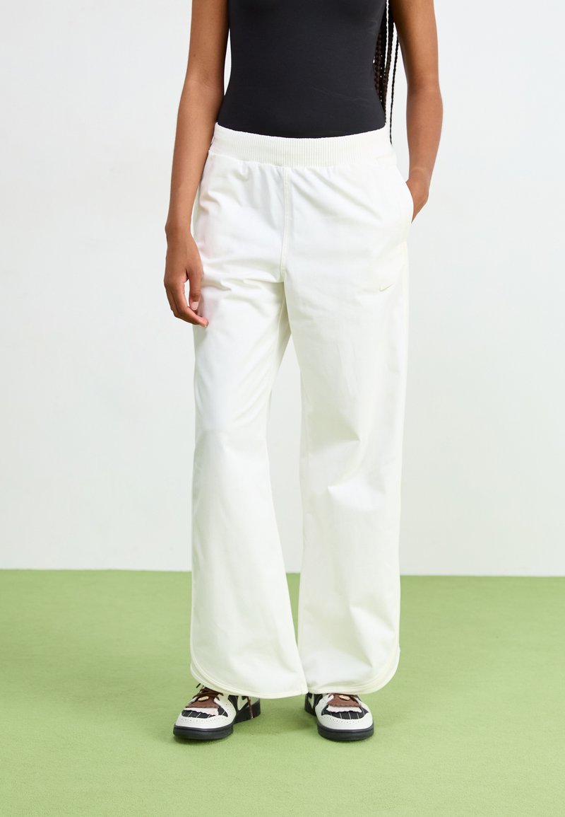 Pantalones blancos de pierna ancha con una cinturilla elástica y una textura suave, combinados con zapatos negros con acentos decorativos.