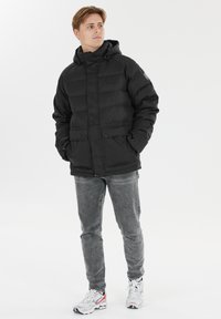 Doudoune noire avec une capuche, présentant un design matelassé, deux poches avant avec rabats et une fermeture éclair. Tissu texturé avec des accents subtils.