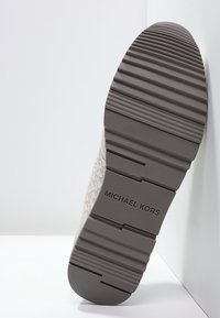 Sneaker z teksturowaną, jasno szaro-zieloną górą, grubą szaro-rubberową podeszwą z poziomymi rowkami oraz wytłoczonym logo marki na pięcie.