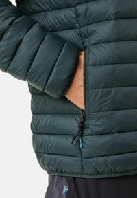 Giacca a vento verde scuro, caratterizzata da una texture trapuntata, tasca con zip e dettagli con coulisse in blu.