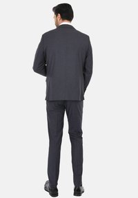 Completo grigio con giacca su misura dalla superficie liscia, pantaloni a gamba dritta e scarpe nere. La vista posteriore mostra linee pulite e cuciture.