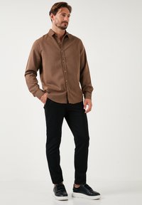 Brun skjorte med knapper i struktureret stof, lange ærmer og spids krave, parret med sorte bukser og sporty sorte sneakers.