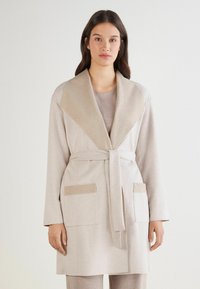 Beżowa szata z kołnierzem szalowym i paskiem. Posiada dwie przednie kieszenie o kontrastowej fakturze. Miękka tkanina, długie rękawy, minimalistyczny design.