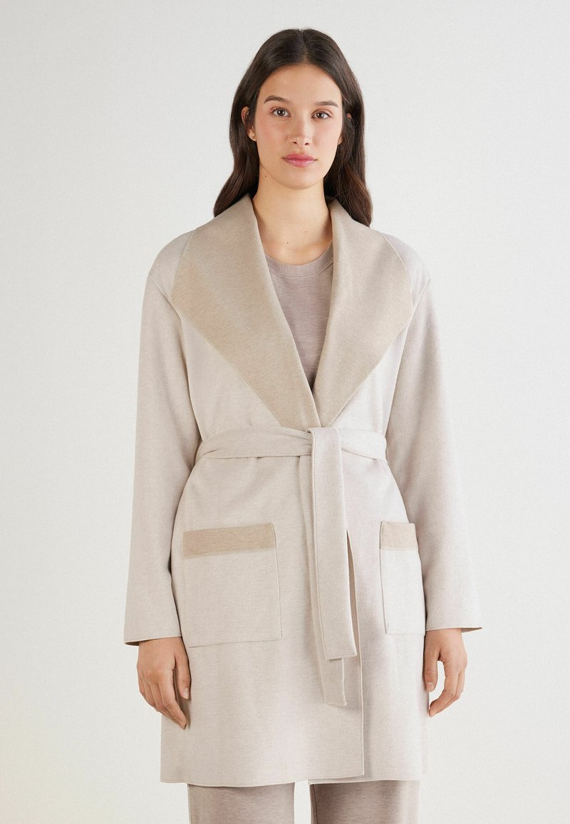 Beżowa szata z kołnierzem szalowym i paskiem. Posiada dwie przednie kieszenie o kontrastowej fakturze. Miękka tkanina, długie rękawy, minimalistyczny design.