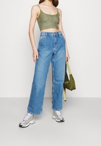 Grön glittrig kort topp, hög midja ljusblå vida jeans, silverfärgade sneakers och en grön handväska med axelrem.