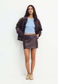 Plommonfärgad faux läderjacka över en ljusblå crop top och en matchande minikjol med knappdetaljer. Modell iförd beige sneakers.