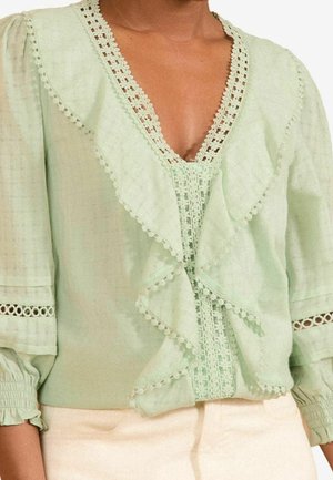 Blusa verde chiaro con rifiniture in pizzo, parte frontale a volant, maniche 3/4 con polsini elasticizzati e un sottile motivo a scacchi nel tessuto.