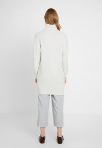 Ljusgrå polotröja med avslappnad passform, kombinerad med rutiga korta byxor och mörkbruna loafers. Mjuk textur, enkel design.