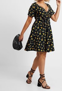 Black floral dress with short sleeves and a twisted front detail. Paired with black strappy sandals and a geometric handbag.