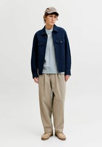Marineblaue, leichte Jacke mit zwei Brusttaschen über einem hellblauen T-Shirt. Lockere beige Hose und beige Mokassins vervollständigen den Look.