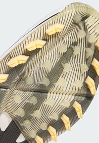 Musta-valkoinen urheilukengän pohja, jossa keltaiset ja läpikuultavat nastat, teksturoidulla pidolla ja kuusikulmaisella kuviolla.