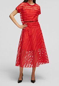 Conjunto rojo de dos piezas que incluye un top de mangas cortas y una falda larga, fabricado con tejido de malla estampada con cortes triangulares.