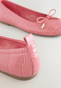 Roosad kunstnahast baleriinajalatsid krokodillinaha mustriga, ümarate varvaste ja esiküljel oleva paelaga. Mugavaks kandmiseks lame kummist tallaosa.