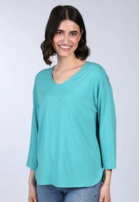 Türkises V-Ausschnitt Langarmshirt aus einem weichen, leichten Stoff, mit einem lockeren Schnitt und seitlichen Schlitzen für zusätzlichen Komfort.