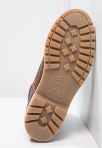 Botte en cuir marron avec une semelle en caoutchouc texturé présentant un motif carré ; le logo sur la semelle indique la marque et l'origine en Espagne.