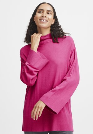 Pull en maille rose à col roulé avec des manches longues et des poignets côtelés, présentant une coupe décontractée et une texture lisse.