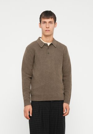 Brown knitted sweater with a collared neck, button detail, and ribbed hem. Worn over a light-coloured shirt and paired with dark checkered trousers.