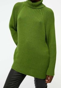 Groene geribbelde gebreide trui met een hoge col, lange mouwen en een ontspannen pasvorm, gecombineerd met zwarte slim-fit broek.